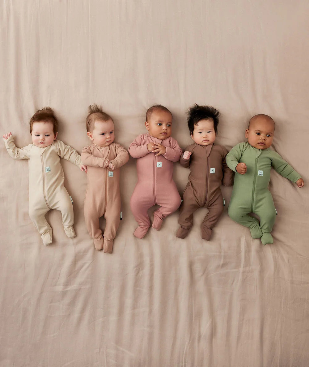 Five babies wearing colorful onesies on a beige blanket