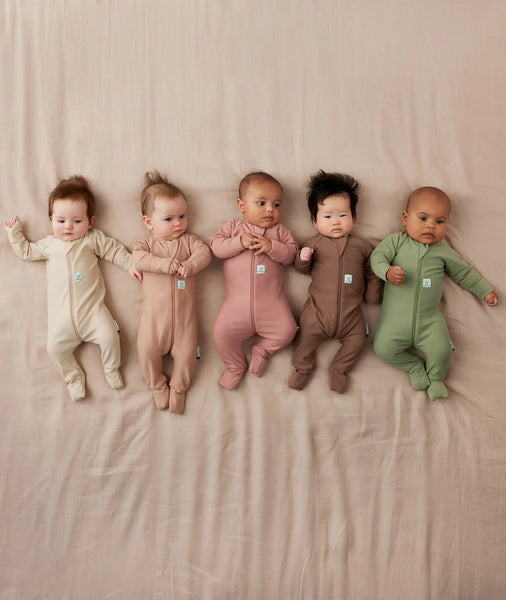 Five babies wearing colorful onesies on a beige blanket