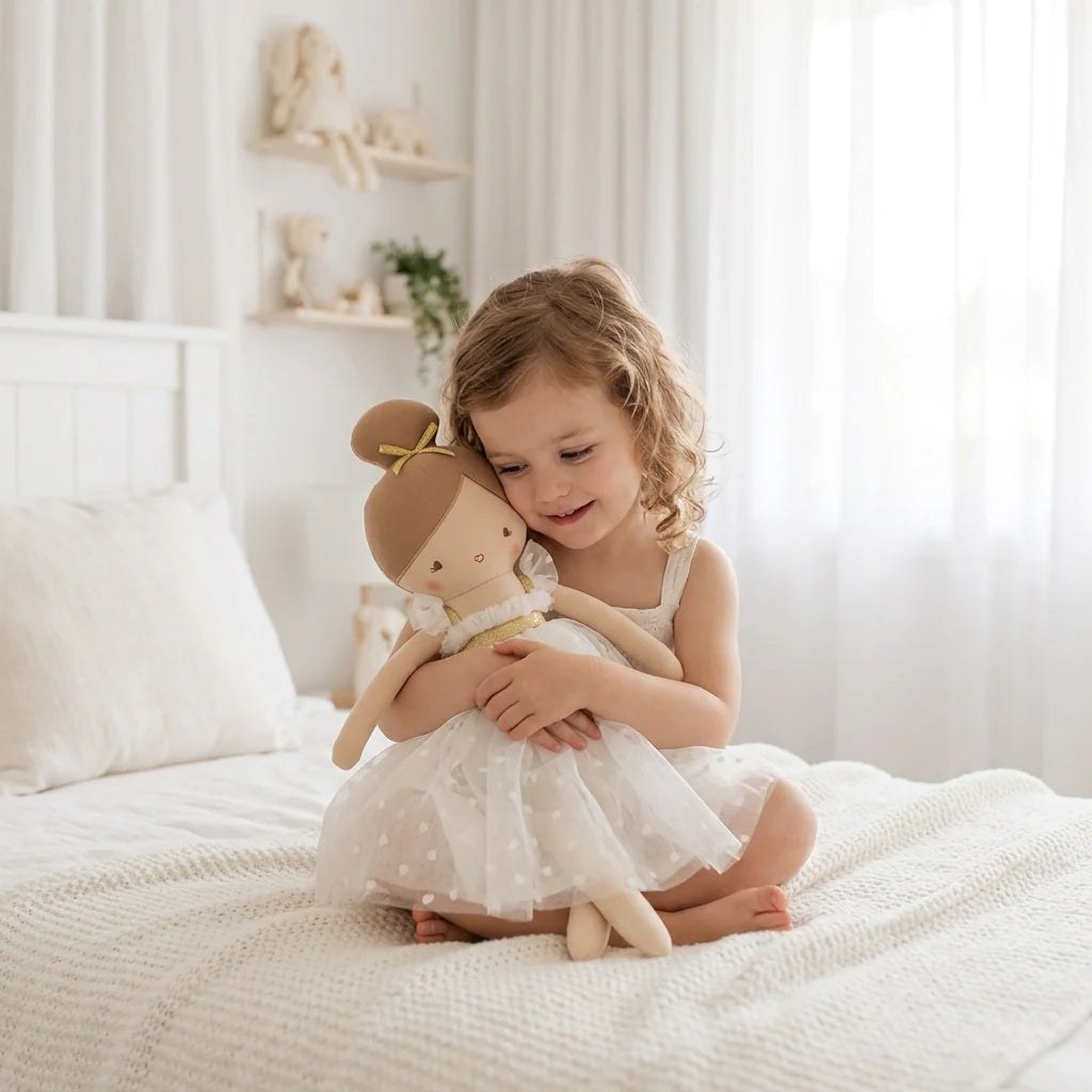 Child in a white dress holding a doll on a bed in a bright room.