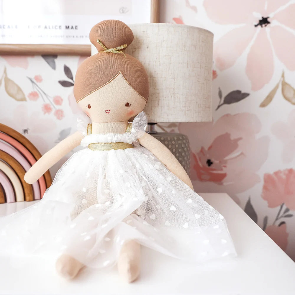 Stuffed doll in a white dress with gold accents against a floral background