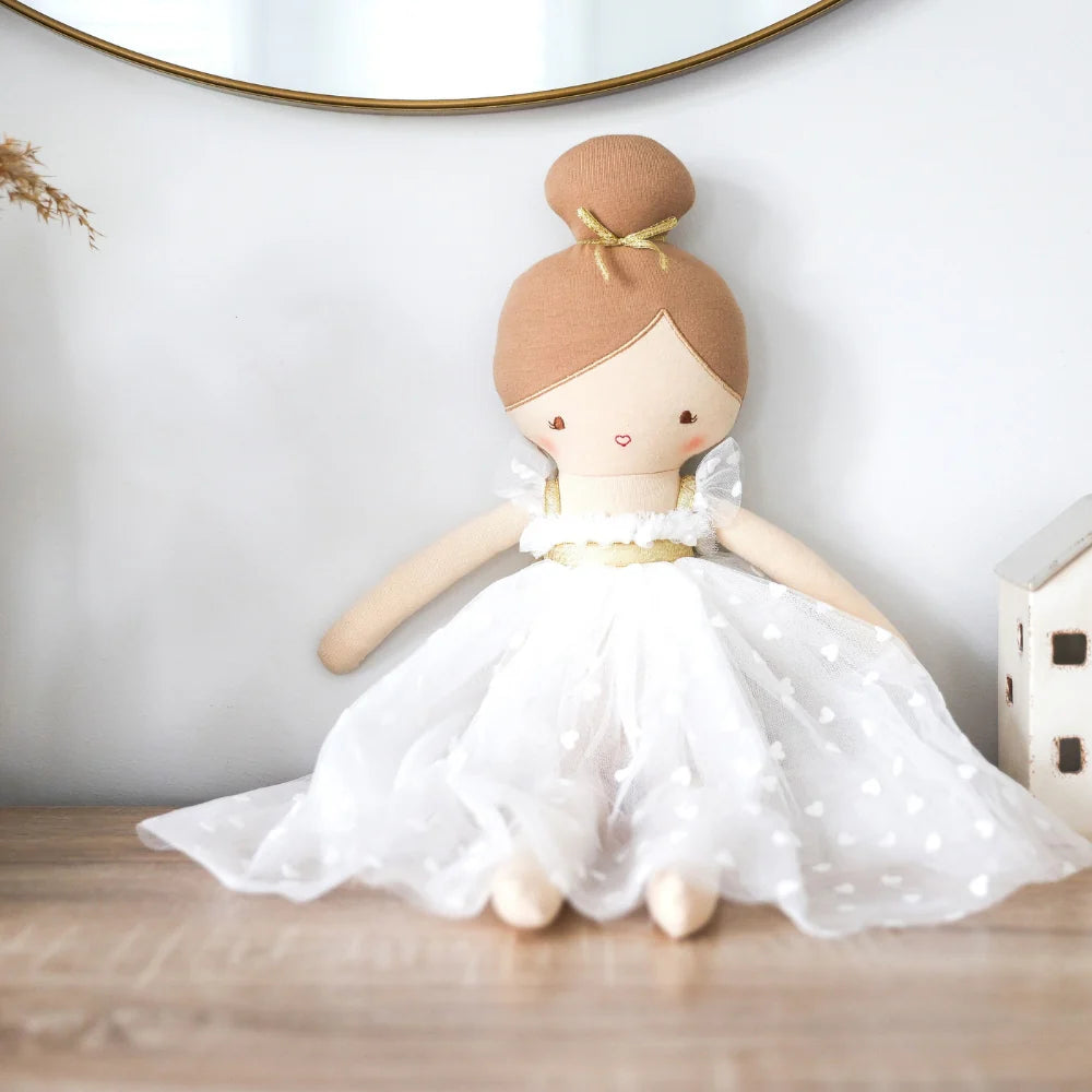 Stuffed doll with brown hair and a white dress on a wooden surface.