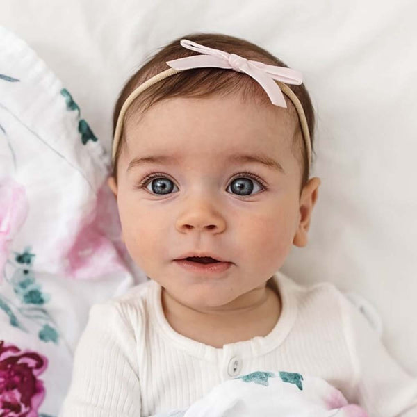 Baby with a pink headband lying on a floral blanket