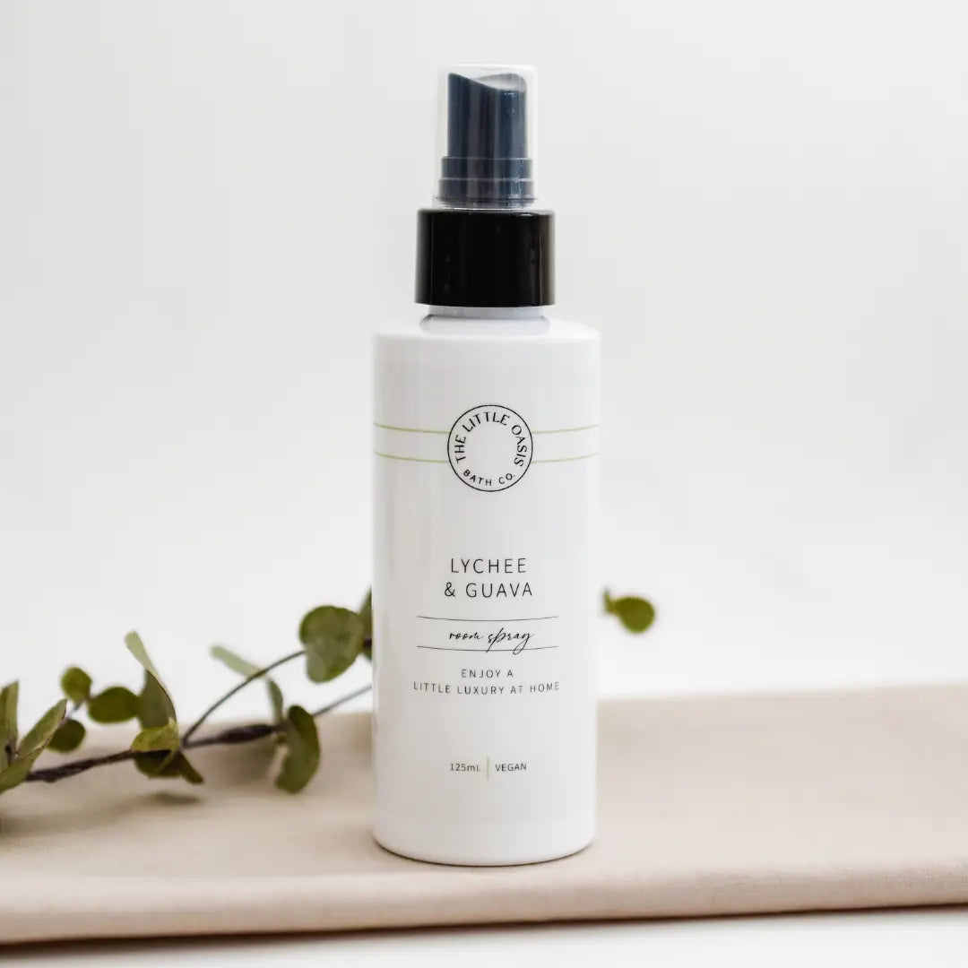 White spray bottle labeled 'Lychee & Guava' on a light background with green leaves.