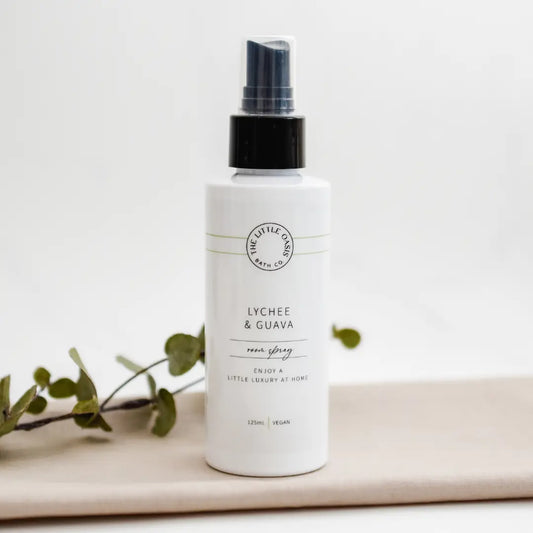 White spray bottle labeled 'Lychee & Guava' on a light background with green leaves.
