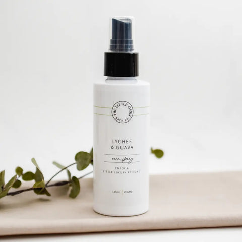 White spray bottle labeled 'Lychee & Guava' on a light background with green leaves.