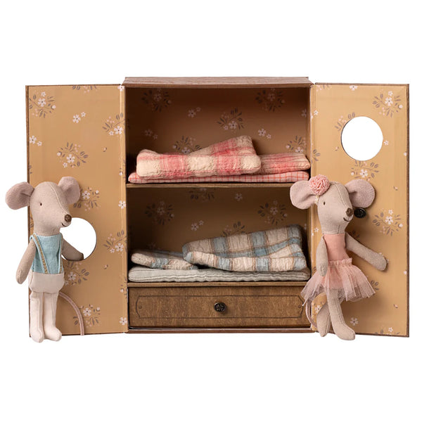 Two plush mouse toys in front of a decorative cabinet with folded cloths inside.