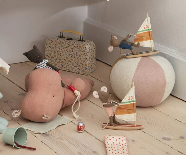 Children's toys including a teddy bear, sailboat, and suitcase on a wooden floor.