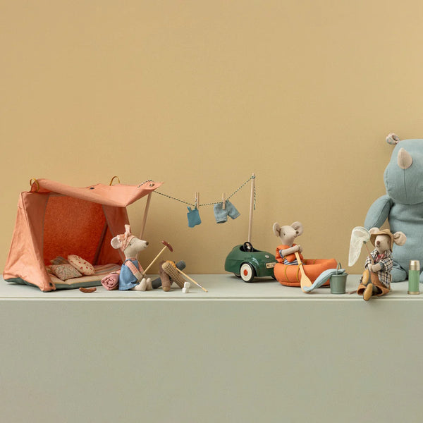 Toy setup with a small tent, car, and figures on a green surface against a beige wall.