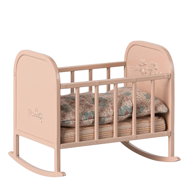 Pink baby crib with floral bedding on a white background