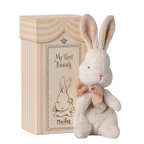 Plush bunny toy with a pink bow in front of a branded box on a white background