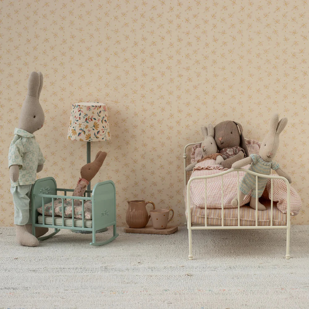 Children's room with stuffed animals on a bed and in a crib, floral wallpaper.