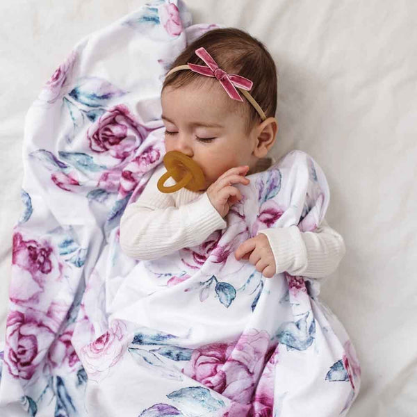 Baby swaddled in a floral blanket with a pacifier, wearing a pink bow.