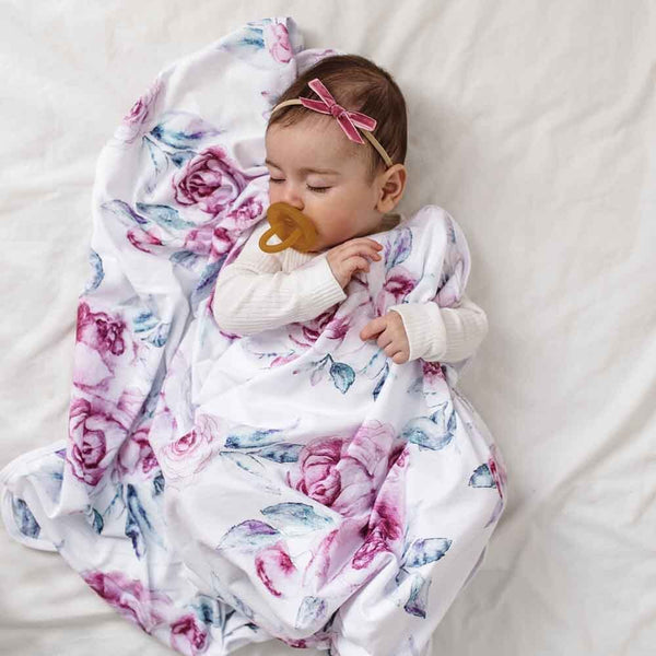 Baby wrapped in a floral blanket with a pacifier, lying on a white surface.