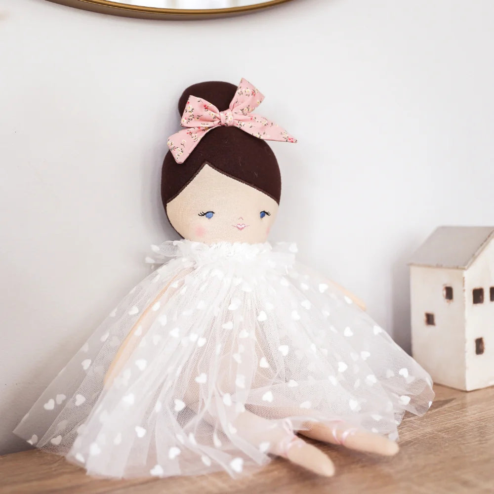 Doll with a white dress and pink bow on a wooden surface