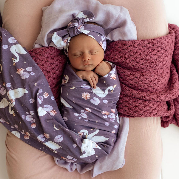 Newborn baby swaddled in a purple blanket with unicorn pattern, wearing a matching headband.