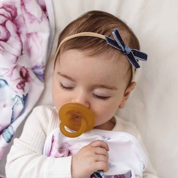 Baby with a pacifier and headband lying on a floral blanket