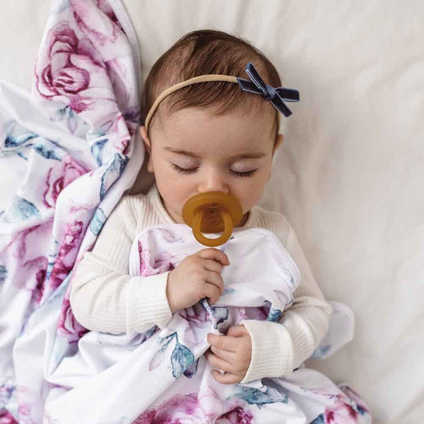 Baby holding a pacifier with floral blanket and white background