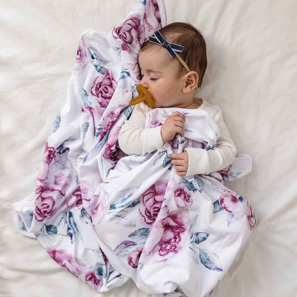 Baby wrapped in a floral blanket with a pacifier, lying on a white surface.