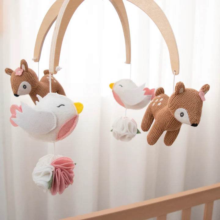 Baby mobile with deer, bird, and flower plush toys hanging from a wooden arch.