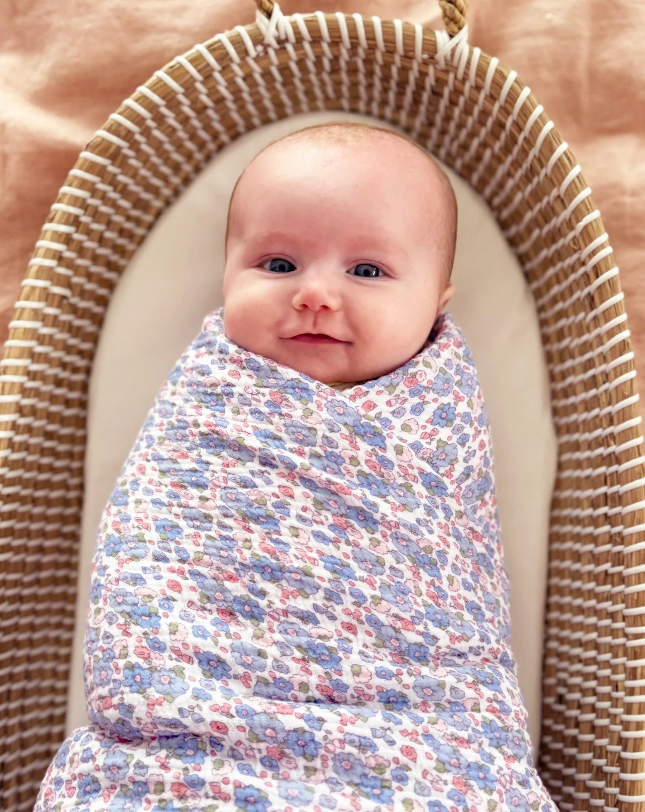 Baby swaddled in a colorful blanket, lying in a woven basket.