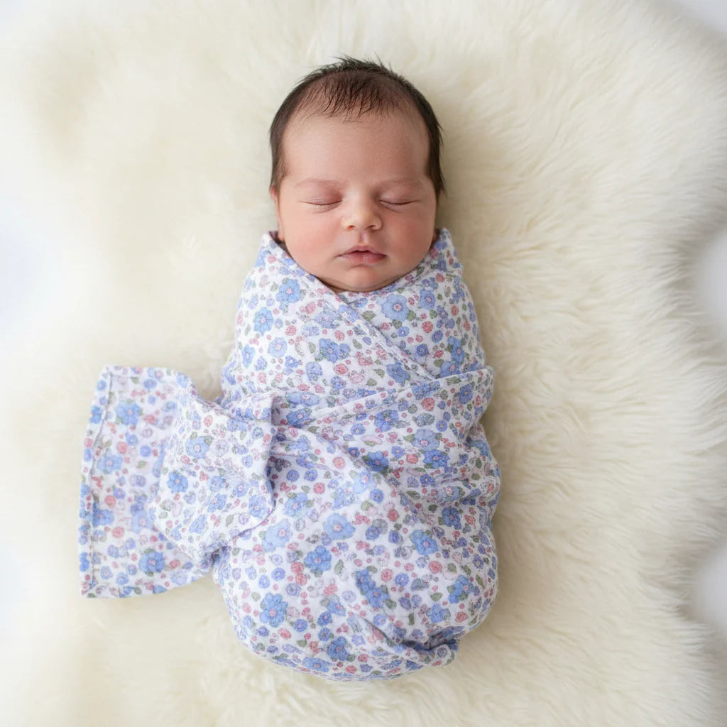 Newborn baby swaddled in a floral blanket on a soft white surface