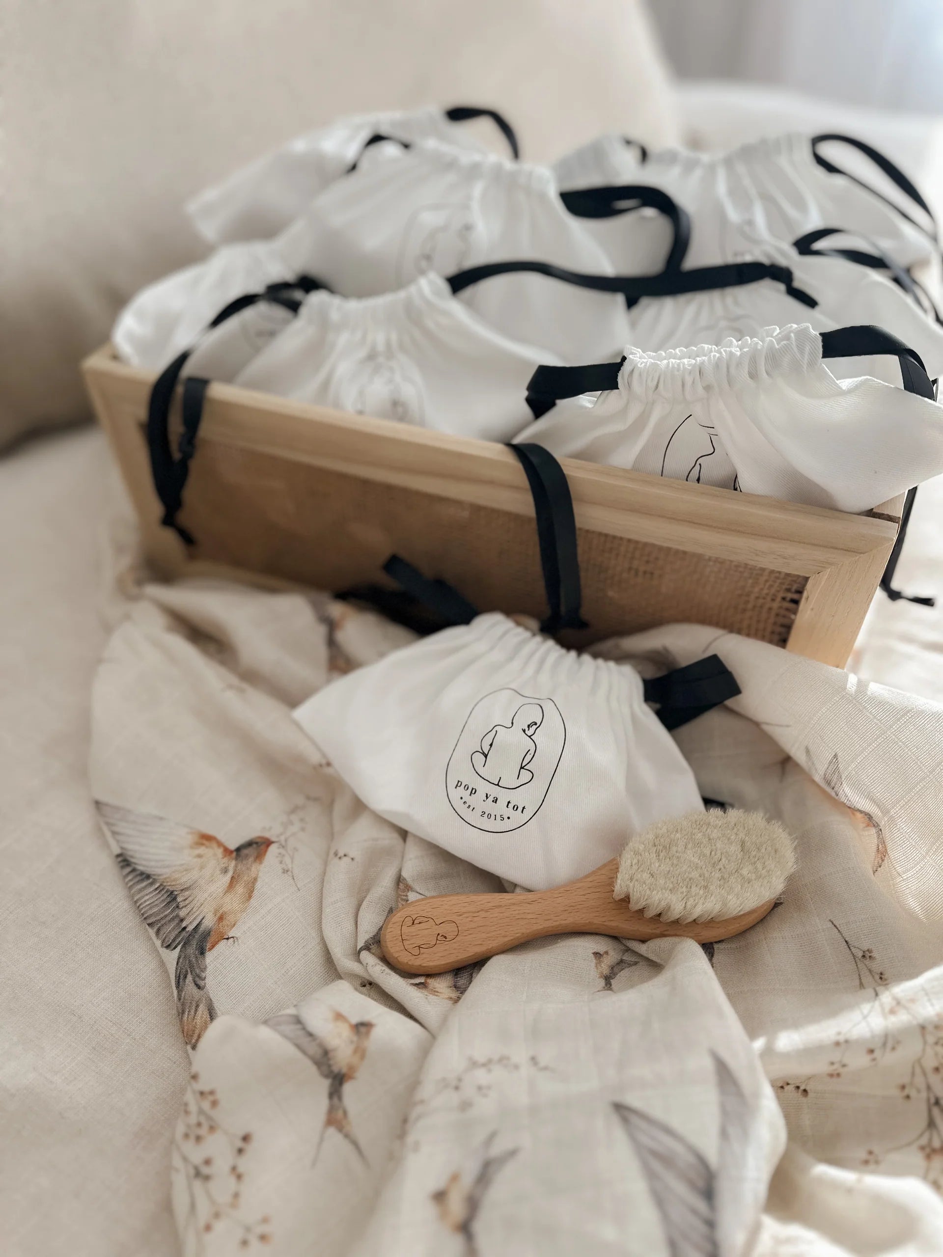 Baby care items including a wooden brush, washcloths, and a box on a soft surface.