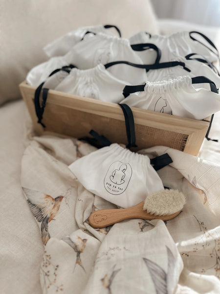 Baby care items including a wooden brush, washcloths, and a box on a soft surface.