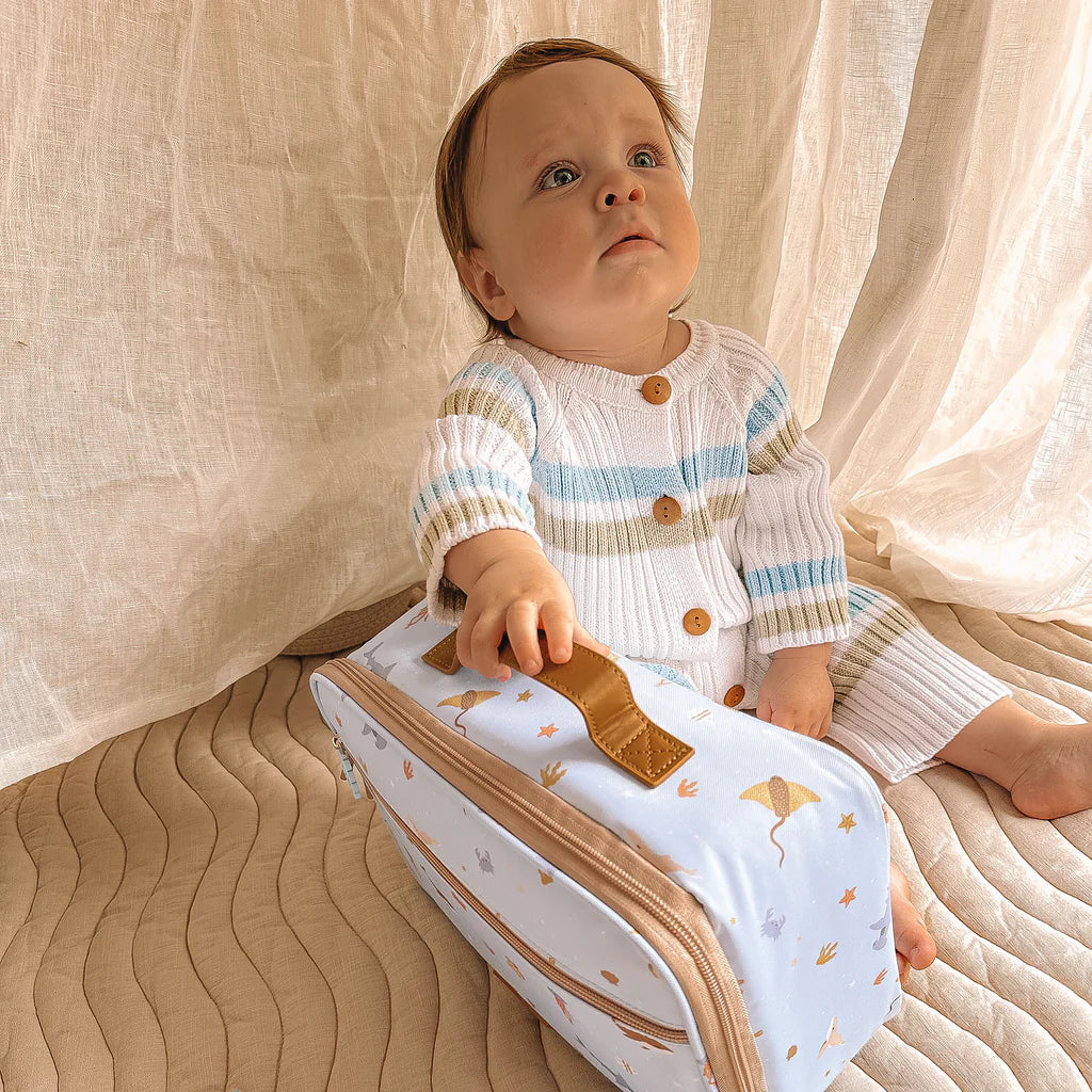 Baby holding a lunch bag with ocean designs against a neutral background