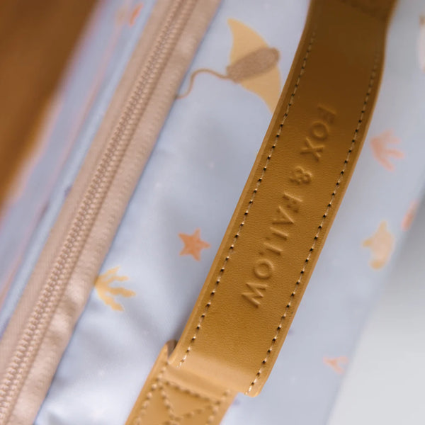 Close-up of a product with a tan strap and zipper, featuring the brand 'Fox & Falcon'.