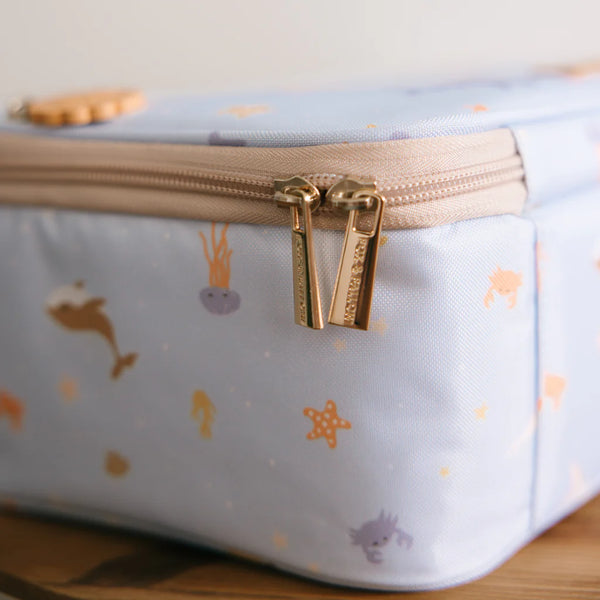 Light blue pouch with gold zipper and sea-themed pattern on a wooden surface