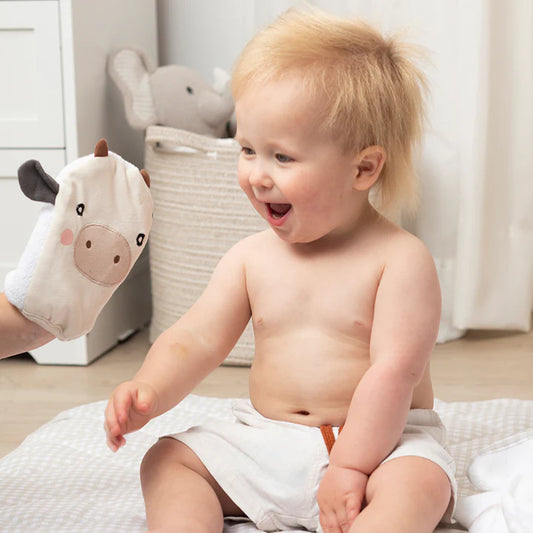Baby sitting on a blanket with a plush toy in a room.