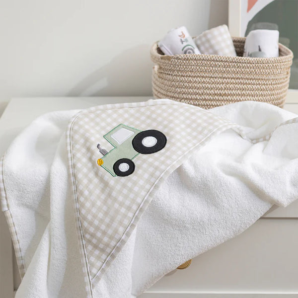 White towel with a green and black tractor applique on a white surface, with a basket in the background.