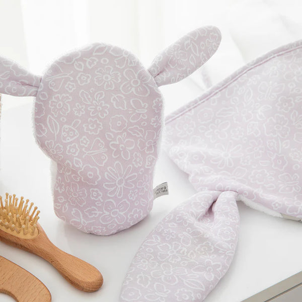 Floral-patterned baby bath mitt and towel set on a white surface with a wooden brush.