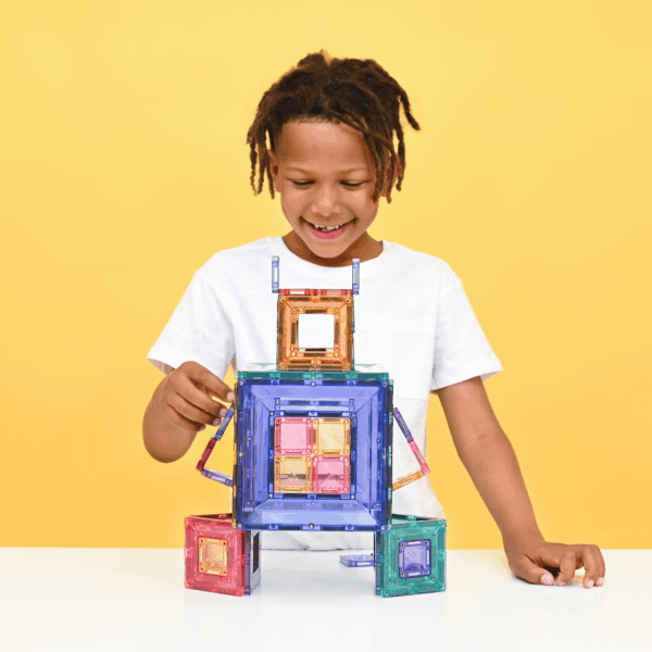 Child playing with colorful magnetic building blocks against a yellow background