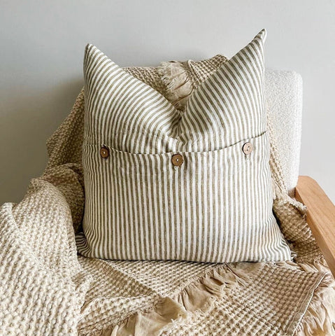 Striped pillow with buttons on a textured blanket against a neutral background