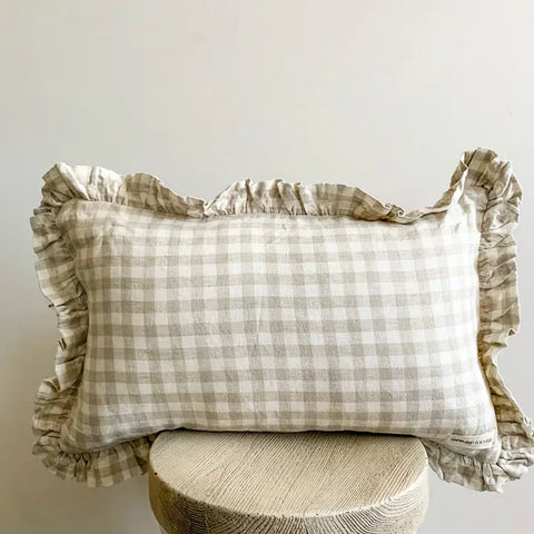 Checkered pillow with ruffled edges on a wooden stool against a plain background