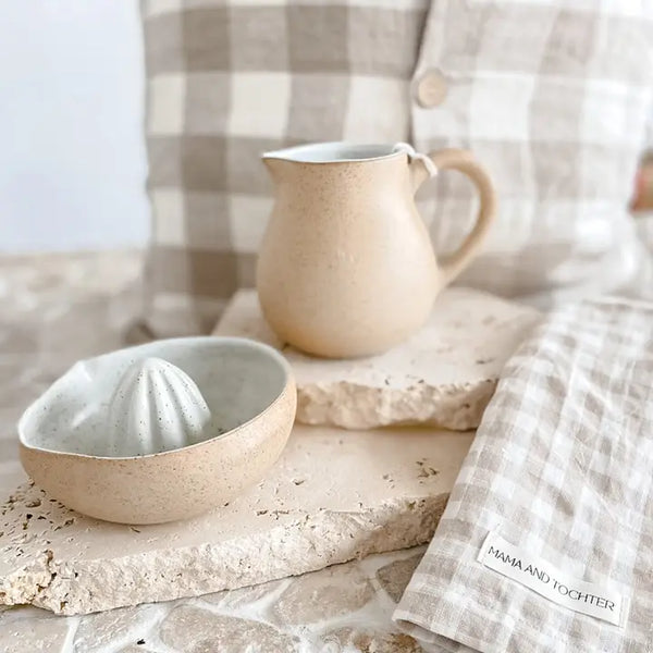 Ceramic pitcher and bowl on a stone surface with a checkered cloth in the background.