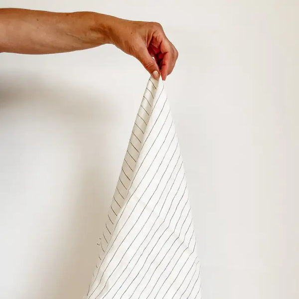 Person holding a white fabric with black stripes against a plain background