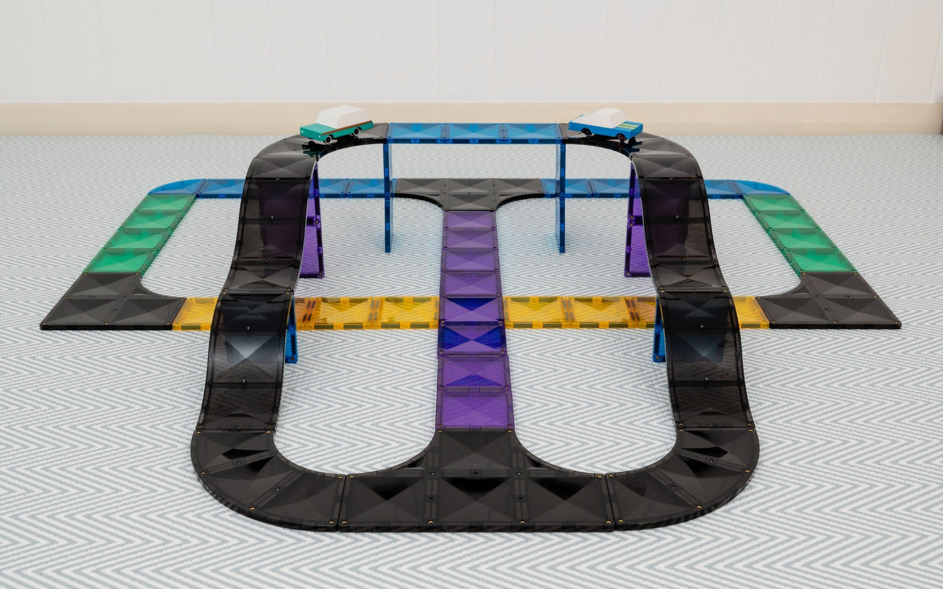 Black toy track with colorful sections on a light gray floor.