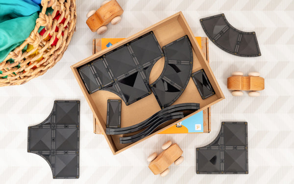 Black geometric toys in a cardboard box on a light surface with wooden toys around.