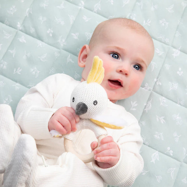 Baby holding a plush toy with a banana-shaped object, lying on a light blue mattress.