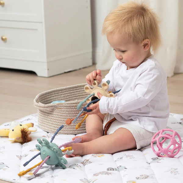 Baby playing with colorful toys on a bed in a nursery setting