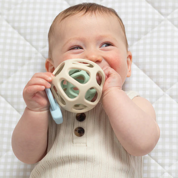 Baby holding a teething ball on a checkered blanket