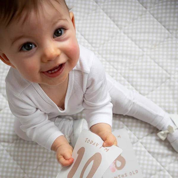 Baby holding a milestone card on a checkered blanket