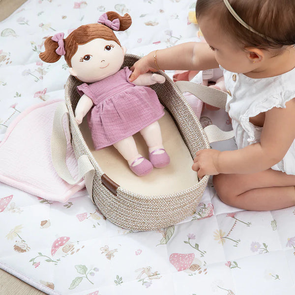 Child playing with a doll in a woven basket on a floral blanket