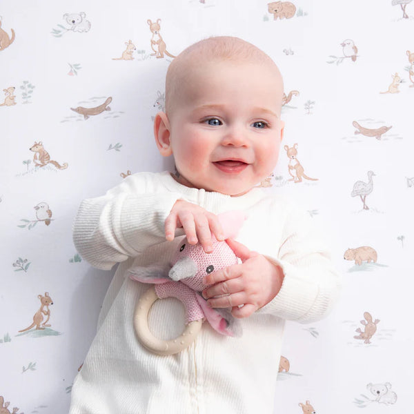 Baby holding a pink toy with a white background featuring animal prints