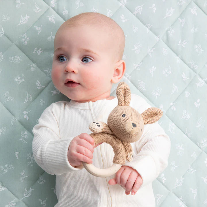 Baby holding a knitted toy with a soft, patterned background