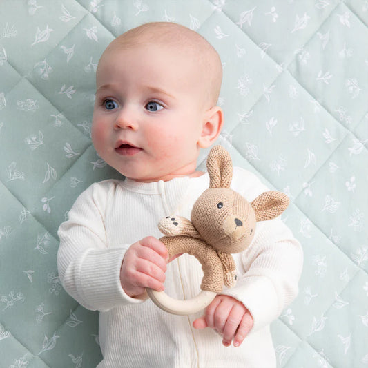 Baby holding a knitted toy with a soft, patterned background