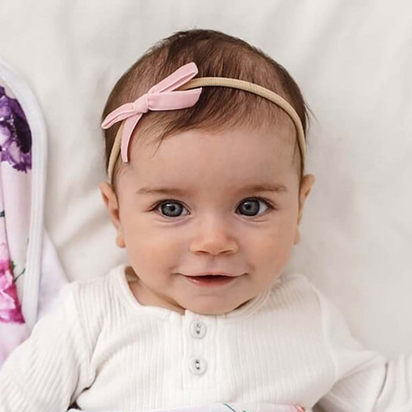 Baby wearing a pink headband with a bow, looking at the camera.