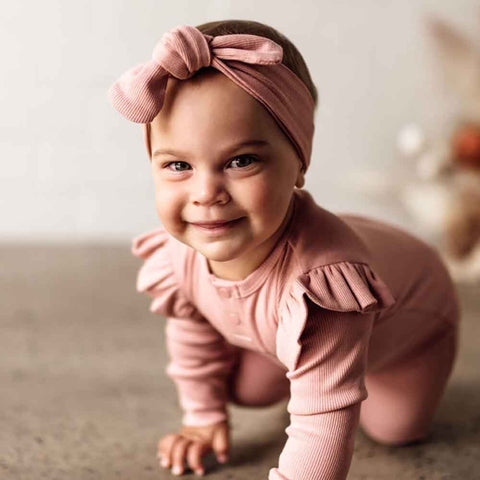 Baby in pink outfit with ruffles and a matching headband, smiling.